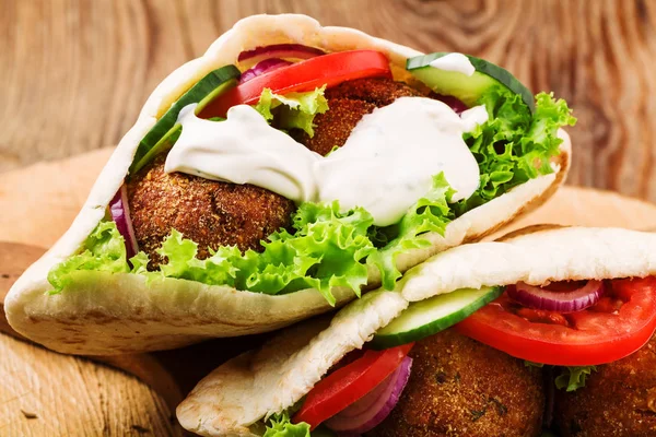 Falafel i świeże warzywa w chlebie pita na drewnianym stole — Zdjęcie stockowe