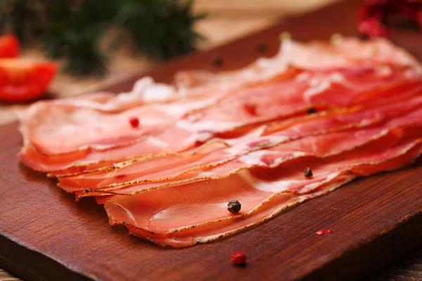 Heerlijke prosciutto ham op een houten bord met specerijen. — Stockfoto