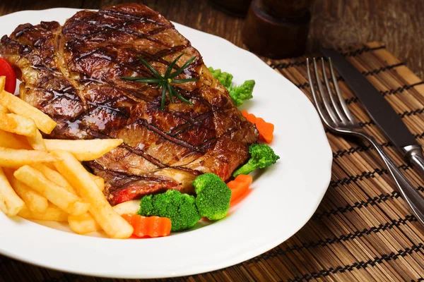 Grilled beef steak served with French fries and vegetables on a — Stock Photo, Image