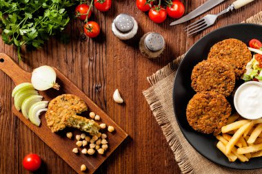 Siyah bir tabakta soslu falafel ve patates kızartması servis ediliyor. Üst Manzara. Tahta arka plan