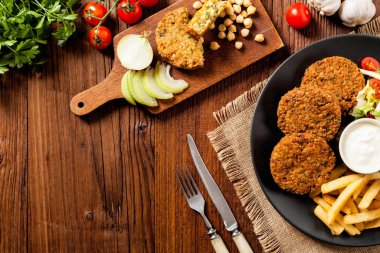 Siyah bir tabakta soslu falafel ve patates kızartması servis ediliyor. Üst Manzara. Tahta arka plan