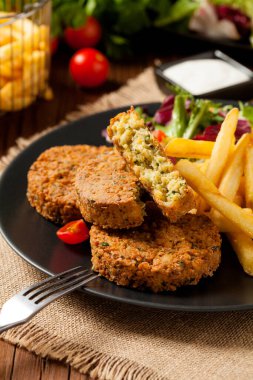 Siyah bir tabakta soslu falafel ve patates kızartması servis ediliyor. Ön görünüm.