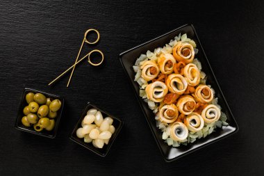 Zeytinli rulo ringa, soğanlı. Votka için mükemmel. Arka planda siyah taş dene. Üst görünüm.