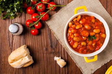 Domates soslu fırınlanmış fasulye, sarı kaselerde servis edilir. Üst görünüm. 