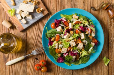 Tofulu, domatesli ve cevizli nefis salata, üzerine balzamik sirke serpilmiş ve mavi bir tabakta servis edilmiş. Ön görünüm.