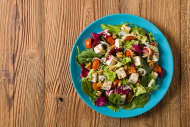 Tofulu, domatesli ve cevizli nefis salata, üzerine balzamik sirke serpilmiş ve mavi bir tabakta servis edilmiş. Ön görünüm.