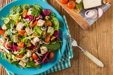 Tofulu, domatesli ve cevizli nefis salata, üzerine balzamik sirke serpilmiş ve mavi bir tabakta servis edilmiş. Ön görünüm.