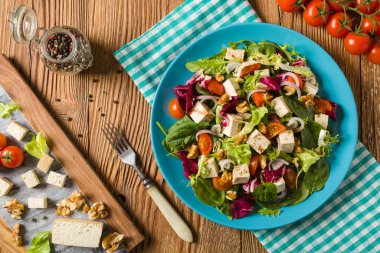 Tofulu, domatesli ve cevizli nefis salata, üzerine balzamik sirke serpilmiş ve mavi bir tabakta servis edilmiş. Ön görünüm.