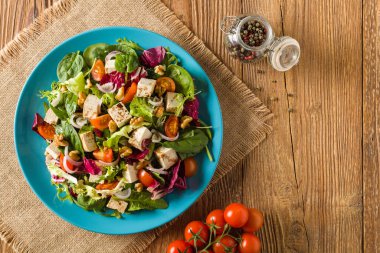 Tofulu, domatesli ve cevizli nefis salata, üzerine balzamik sirke serpilmiş ve mavi bir tabakta servis edilmiş. Ön görünüm.