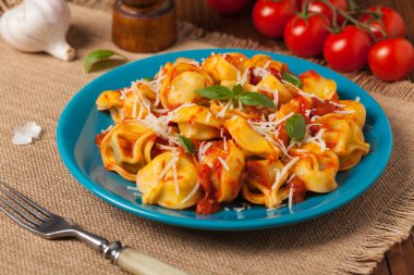 Domates soslu leziz tortellini, üzerine parmesan peyniri ve fesleğen serpiştirilmiş. Ön görünüm.