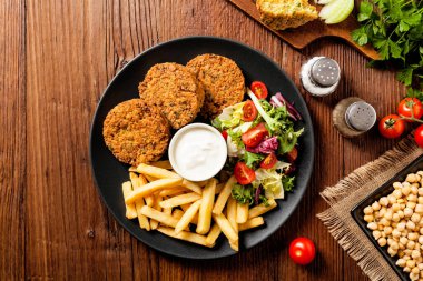 Siyah bir tabakta soslu falafel ve patates kızartması servis ediliyor. Üst Manzara. Tahta arka plan