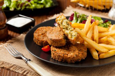 Siyah bir tabakta soslu falafel ve patates kızartması servis ediliyor. Ön görünüm.