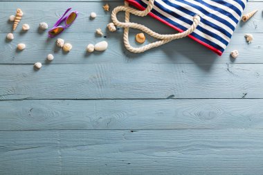 Yaz tatili teması deniz kabukları, çanta, şapka, güneş gözlüğü ve fotokopi alanı olan mavi ahşap arka plan. Üst görünüm.