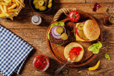 Ev yapımı, peynirli ve sebzeli sığır burger. Patates kızartmasıyla servis edilmiş. Üst görünüm.