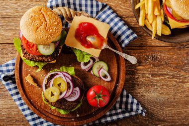 Ev yapımı, peynirli ve sebzeli sığır burger. Patates kızartmasıyla servis edilmiş. Üst görünüm.