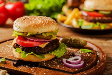 Ev yapımı, peynirli ve sebzeli sığır burger. Patates kızartmasıyla servis edilmiş. Ön görünüm.