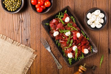 Biftek carpaccio mozzarella peyniri, roka ve kapari ile servis edilir. Üst görünüm.