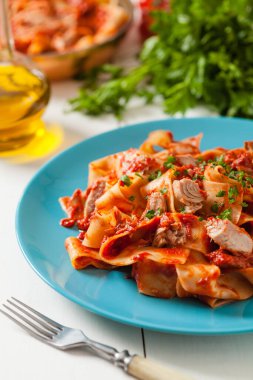 Domates soslu ton balıklı Tagliatelle makarnası. Mavi tabakta servis edilmiş, arka planda beyaz panolar. Ön görünüm. 