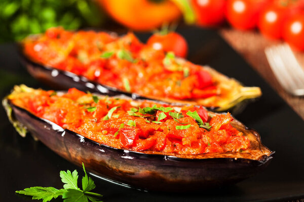 Stuffed aubergine on black plate. Wooden background. Front view.