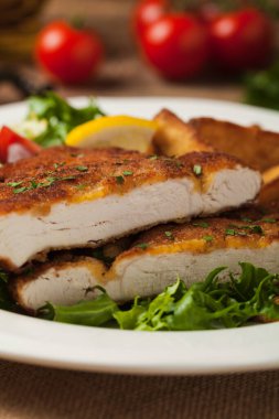 Kızarmış patates ve salatayla servis edilen tavuk şnitzel. Ön manzara. Doğal ahşap zemin