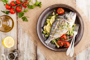 Fırında balık, kızarmış sebze ve limonla servis ediliyor. Üst görünüm.