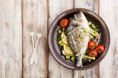 Fırında balık, kızarmış sebze ve limonla servis ediliyor. Üst görünüm.