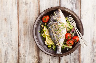 Fırında balık, kızarmış sebze ve limonla servis ediliyor. Üst görünüm.