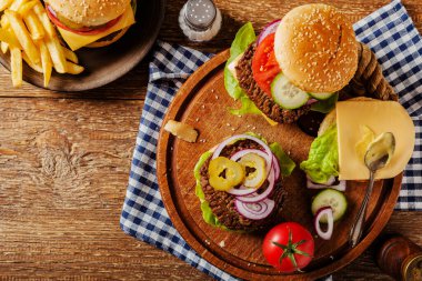 Ev yapımı, peynirli ve sebzeli sığır burger. Patates kızartmasıyla servis edilmiş. Üst görünüm.