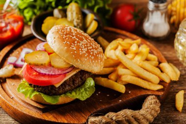 Ev yapımı, peynirli ve sebzeli sığır burger. Patates kızartmasıyla servis edilmiş. Ön görünüm.