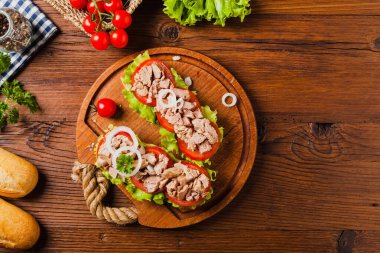 Lezzetli ton balıklı sandviç, marul, domates ve soğanlı. Arka planda doğal ahşap. Üst görünüm.