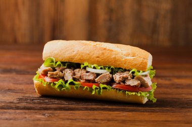 Lezzetli ton balıklı sandviç, marul, domates ve soğanlı. Arka planda doğal ahşap. Ön görünüm.