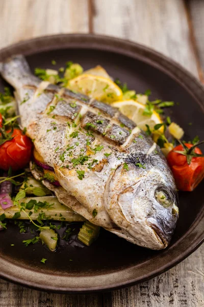 Fırında balık, kızarmış sebze ve limonla servis ediliyor. Ön görünüm.