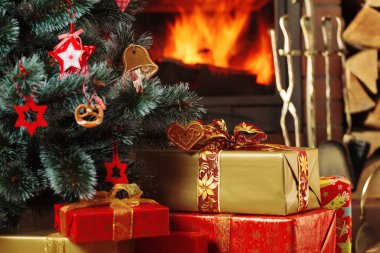 Kükreyen bir şöminenin arkasında Noel ağacının altında hediyeler..