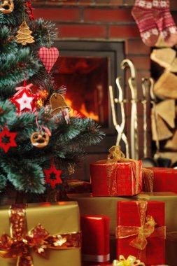 Kükreyen bir şöminenin arkasında Noel ağacının altında hediyeler..