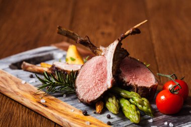 Fırında kuzu fileto, kuşkonmazla servis edilir. Koyu arkaplan.