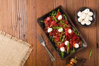 Biftek carpaccio mozzarella peyniri, roka ve kapari ile servis edilir. Üst görünüm.