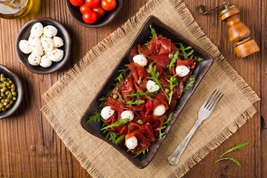 Biftek carpaccio mozzarella peyniri, roka ve kapari ile servis edilir. Üst görünüm.