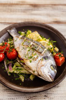 Fırında balık, kızarmış sebze ve limonla servis ediliyor. Ön görünüm.