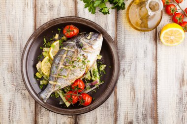 Fırında balık, kızarmış sebze ve limonla servis ediliyor. Üst görünüm.