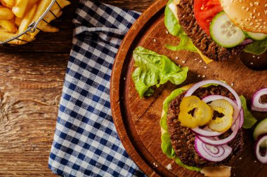 Ev yapımı, peynirli ve sebzeli sığır burger. Patates kızartmasıyla servis edilmiş. Üst görünüm.