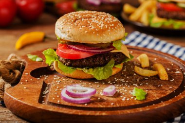 Ev yapımı, peynirli ve sebzeli sığır burger. Patates kızartmasıyla servis edilmiş. Ön görünüm.