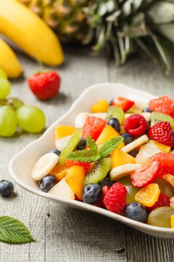 Taze meyveli lezzetli meyve salatası. Arkadaki tahta, gri masa. Ön görünüm.