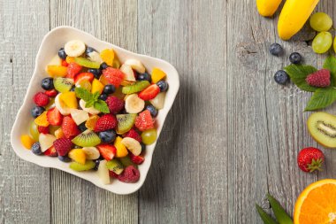 Taze meyveli lezzetli meyve salatası. Arkadaki tahta, gri masa. Üst görünüm.