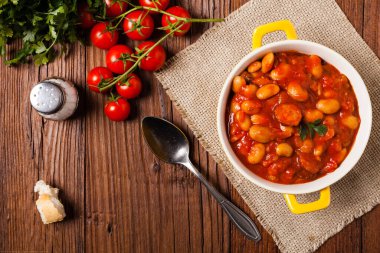 Domates soslu fırınlanmış fasulye, sarı kaselerde servis edilir. Üst görünüm. 