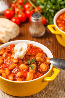 Domates soslu fırınlanmış fasulye, sarı kaselerde servis edilir. Ön görünüm. 