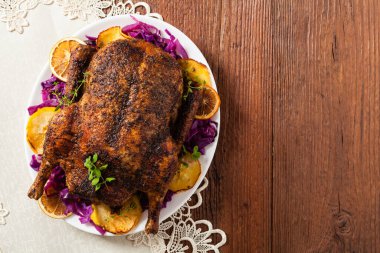 Fırında ördek, elma, kırmızı lahana, portakal ve kızarmış börek ile servis edilir. Arka planda doğal ahşap masa. Üst görünüm.