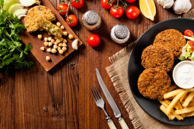 Siyah bir tabakta soslu falafel ve patates kızartması servis ediliyor. Üst Manzara. Tahta arka plan
