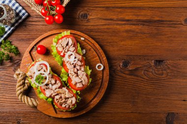 Lezzetli ton balıklı sandviç, marul, domates ve soğanlı. Arka planda doğal ahşap. Üst görünüm.