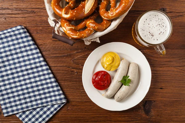 Boiled white sausages, served with beer and pretzels. Perfect for Octoberfest. Natural wooden background. Top view.