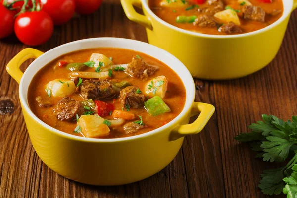 Beef stew served with cooked potatoes in a yellow little pot on a wooden background.